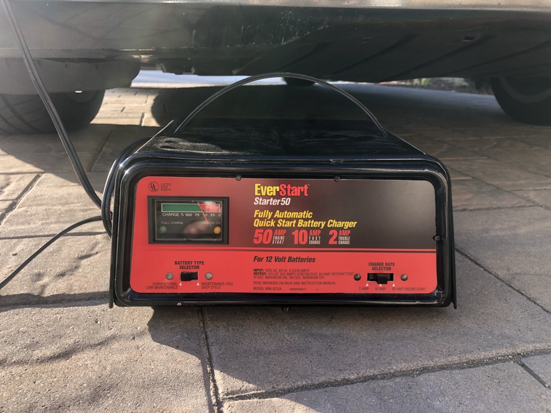 NOCO GENIUS5 smart battery charger connected to a car battery in a workshop