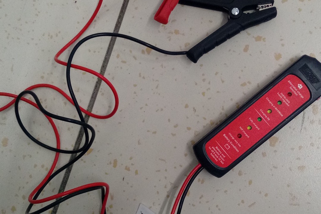 ANCEL BA101 12V automotive battery tester clamped to a car battery on a workbench