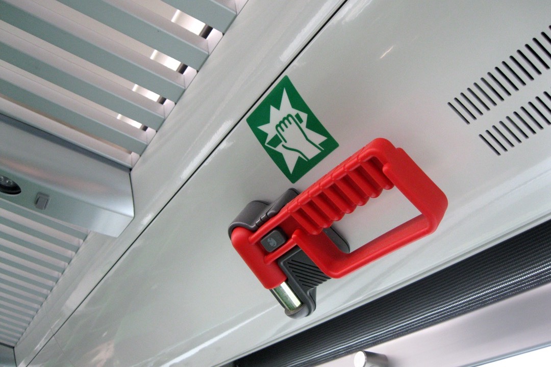 Red emergency window-breaking hammer mounted in a vehicle interior next to a passenger window