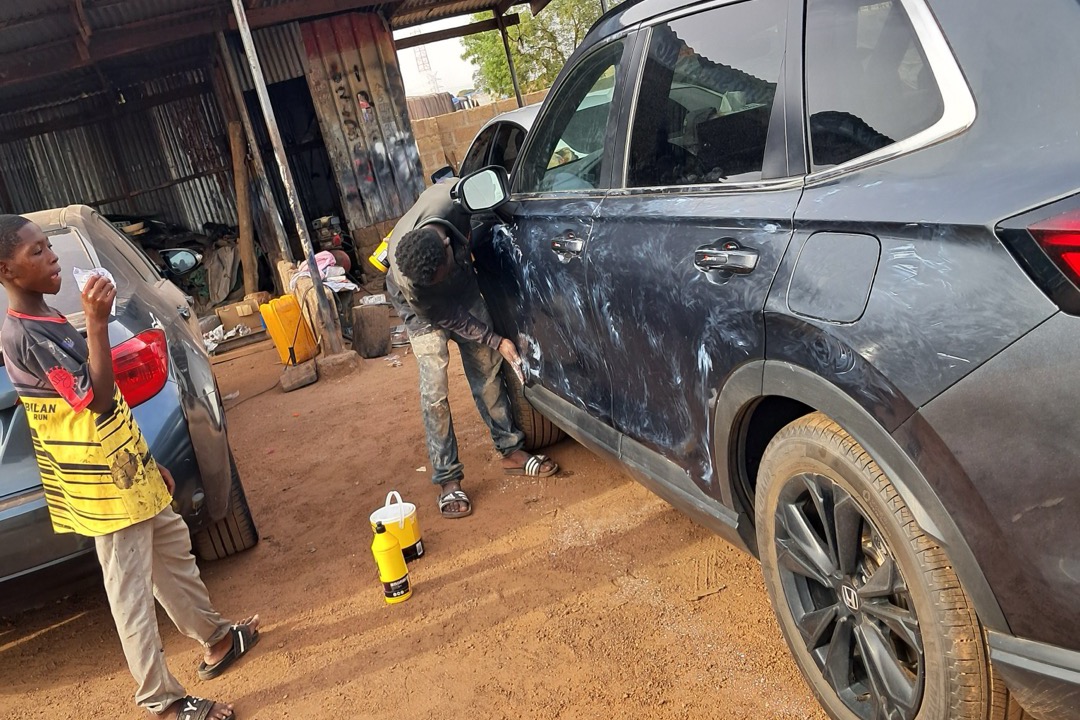 Dual-action car polisher with orange foam pad on a black hood reflecting workshop lights