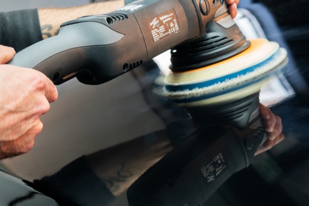 DA polisher with microfiber pad being used to correct paint on a glossy black car panel