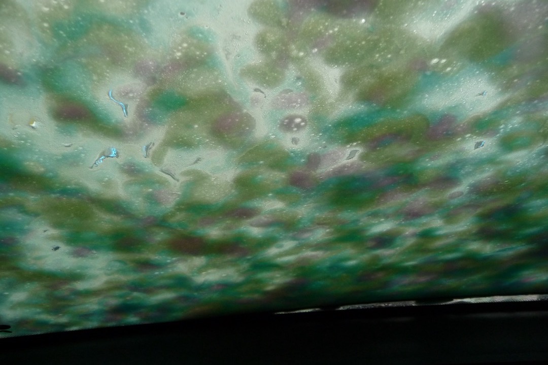 Foam cannon producing thick white suds on a black car hood during a hand wash