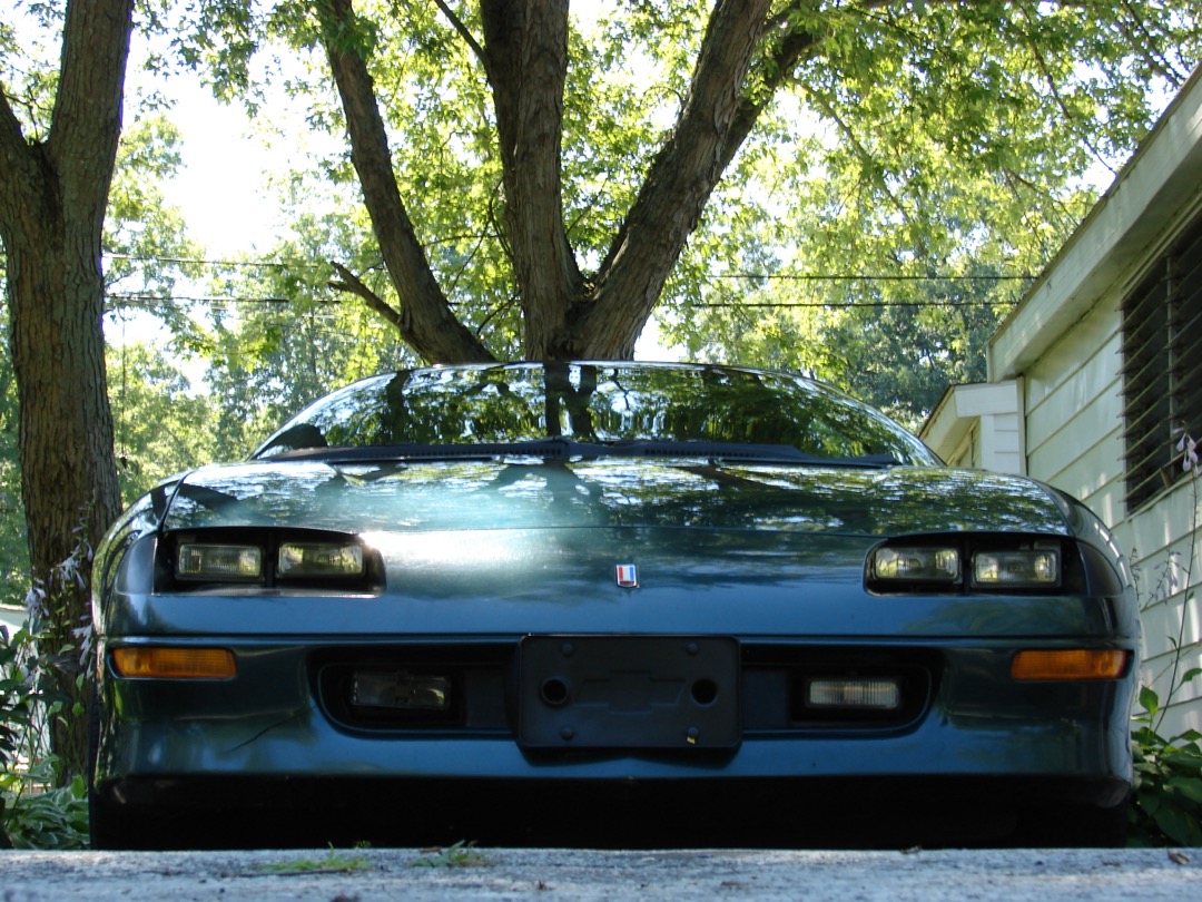 Hand applying car wax to a glossy red hood panel with a foam applicator pad