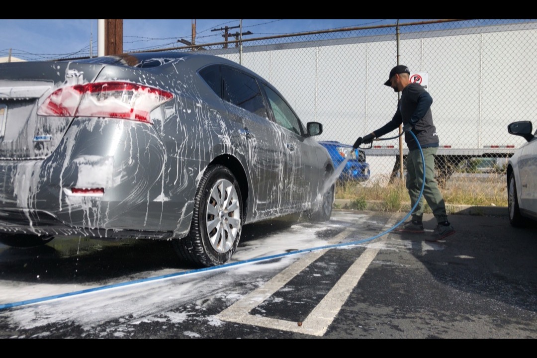 Hand running a yellow clay bar over a glossy black car hood with detailing lubricant