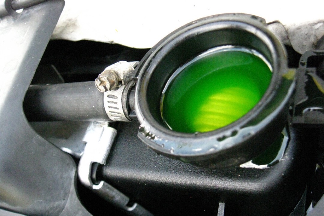 Gallon jug of automotive coolant antifreeze next to a car radiator cap in an engine bay