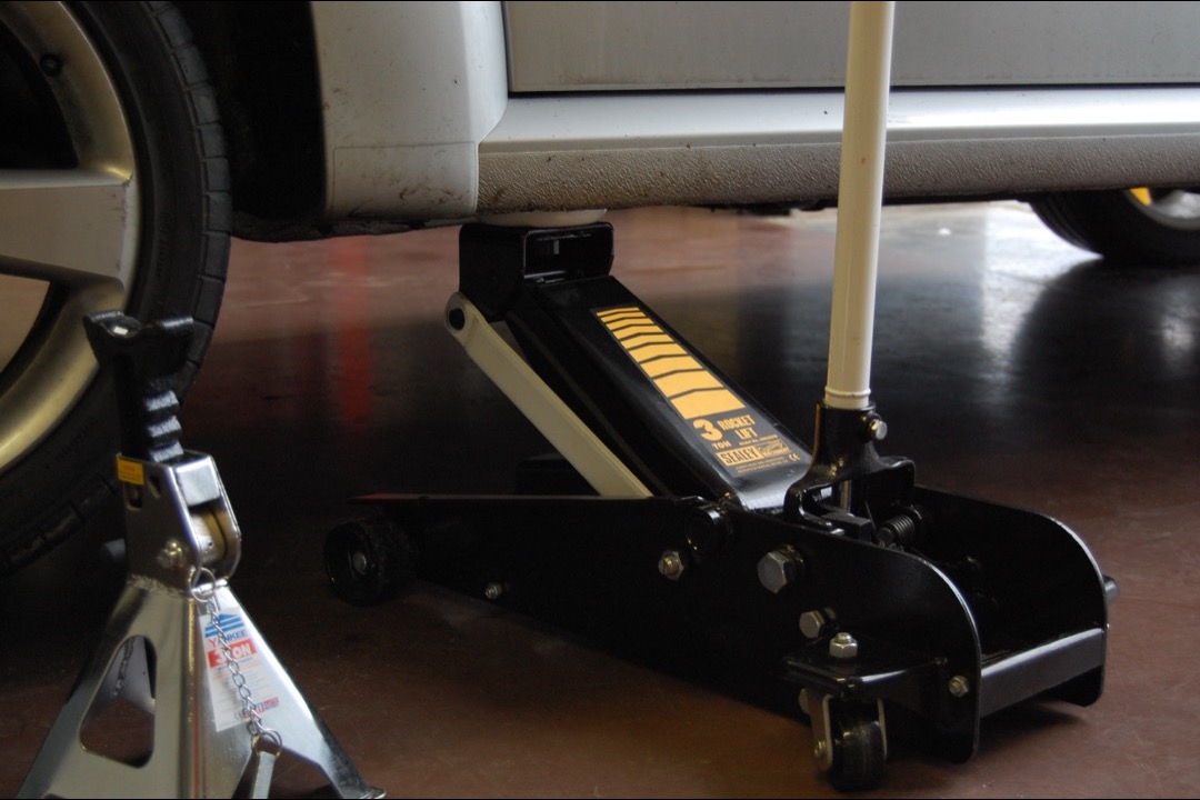 Professional hydraulic floor jack positioned under a vehicle frame in a garage