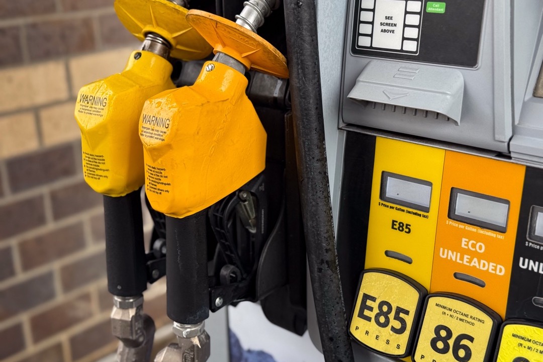 Bottle of fuel stabilizer being added to a gas can next to a stored motorcycle in a garage