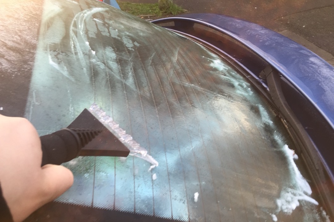 Hand using an ice scraper to clear frost from a frozen car window