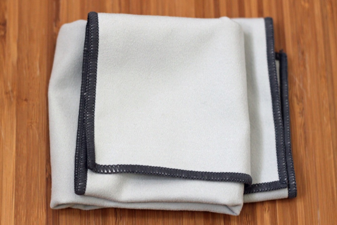 Stack of folded microfiber towels in multiple colors next to a bottle of ceramic spray on a glossy black hood