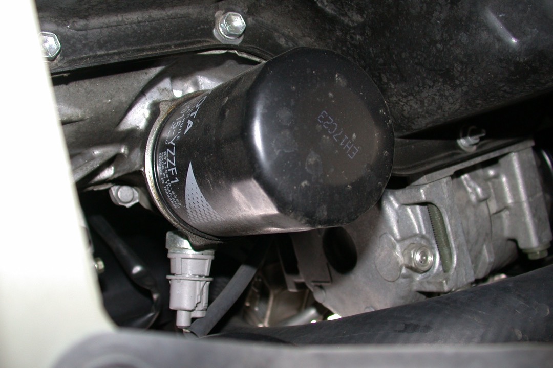 Spin-on oil filter being inspected next to a car engine in a workshop