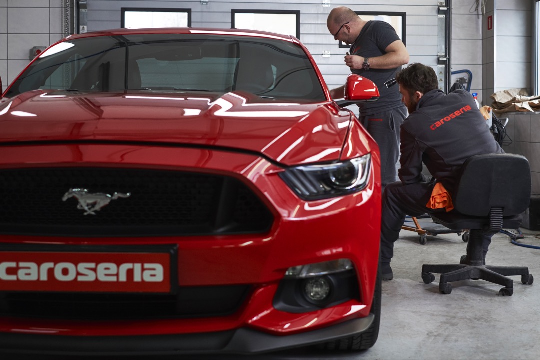 Clear paint protection film being installed on a vehicle hood with a squeegee tool