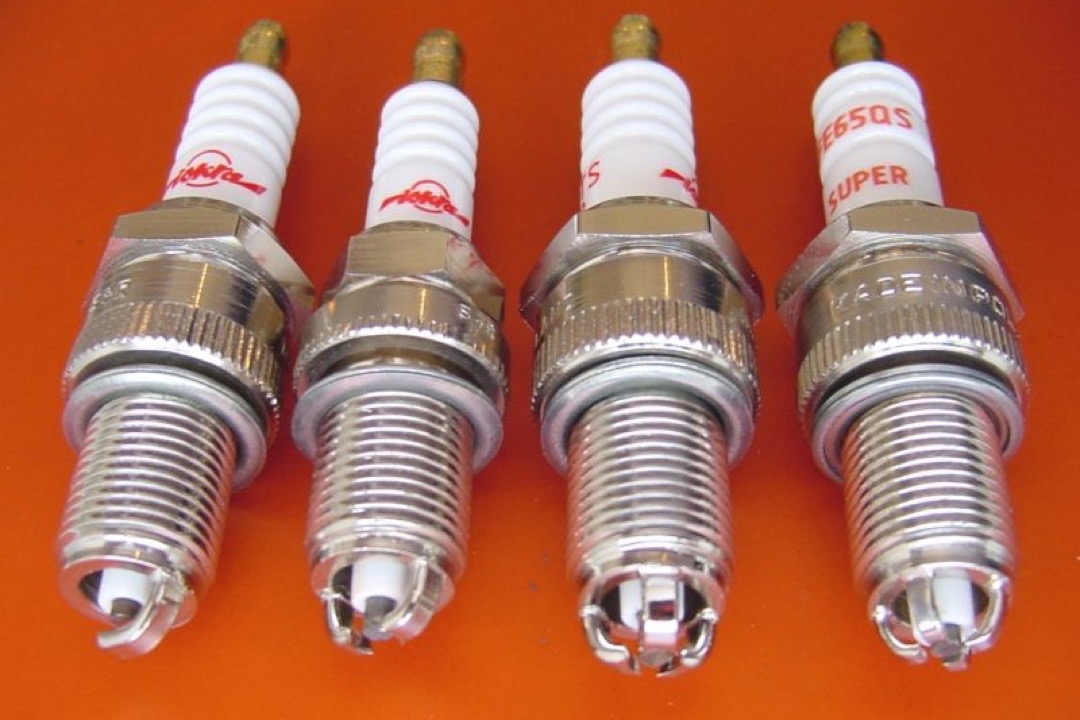 Close-up of an iridium spark plug showing the fine-wire center electrode and ground strap against a workshop background