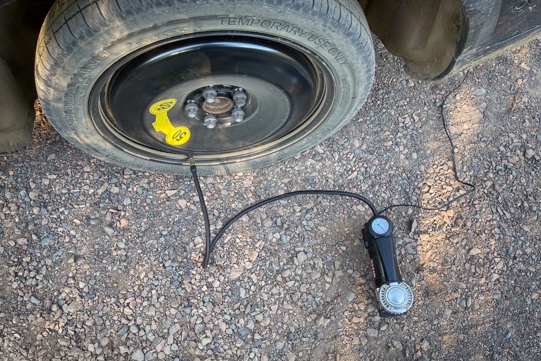 Portable cordless tire inflator connected to a car tire valve stem on a vehicle wheel