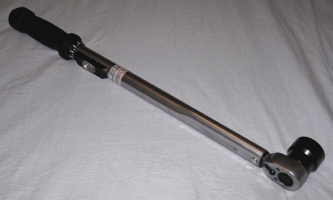 Chrome click-type torque wrench laid on a metal workbench next to sockets and fasteners in an automotive shop