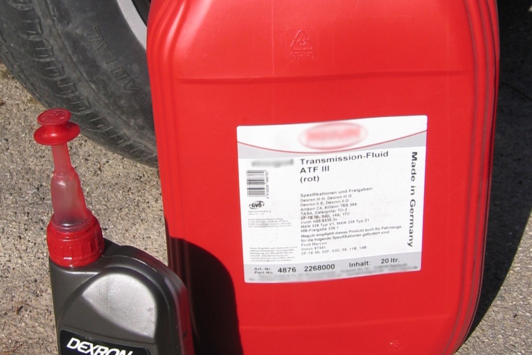 Quart bottles of automatic transmission fluid lined up next to a dipstick and funnel on a shop bench