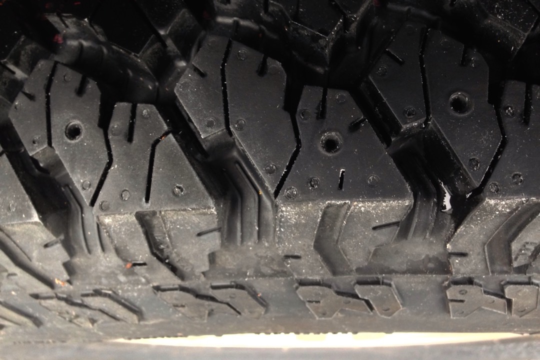 Winter tire mounted on a wheel being inspected in an automotive shop with snow visible through the garage door