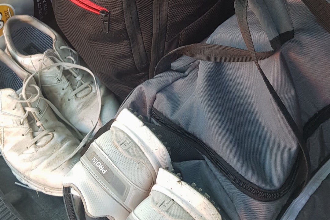 Golf trunk organizer with ventilated shoe compartments and divided storage sitting in the cargo area of a car alongside a golf bag