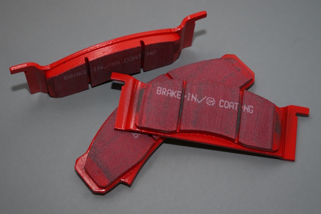 A pair of new red-coated automotive disc brake pads laid on a grey studio background, friction material facing up