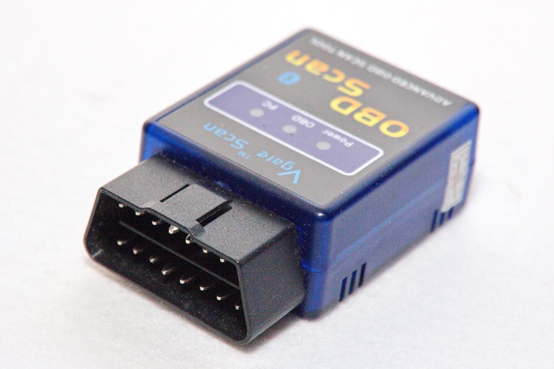 An OBD2 scan tool plugged into a vehicle's diagnostic port under the dashboard, displaying a trouble code on its screen during a diagnostic session