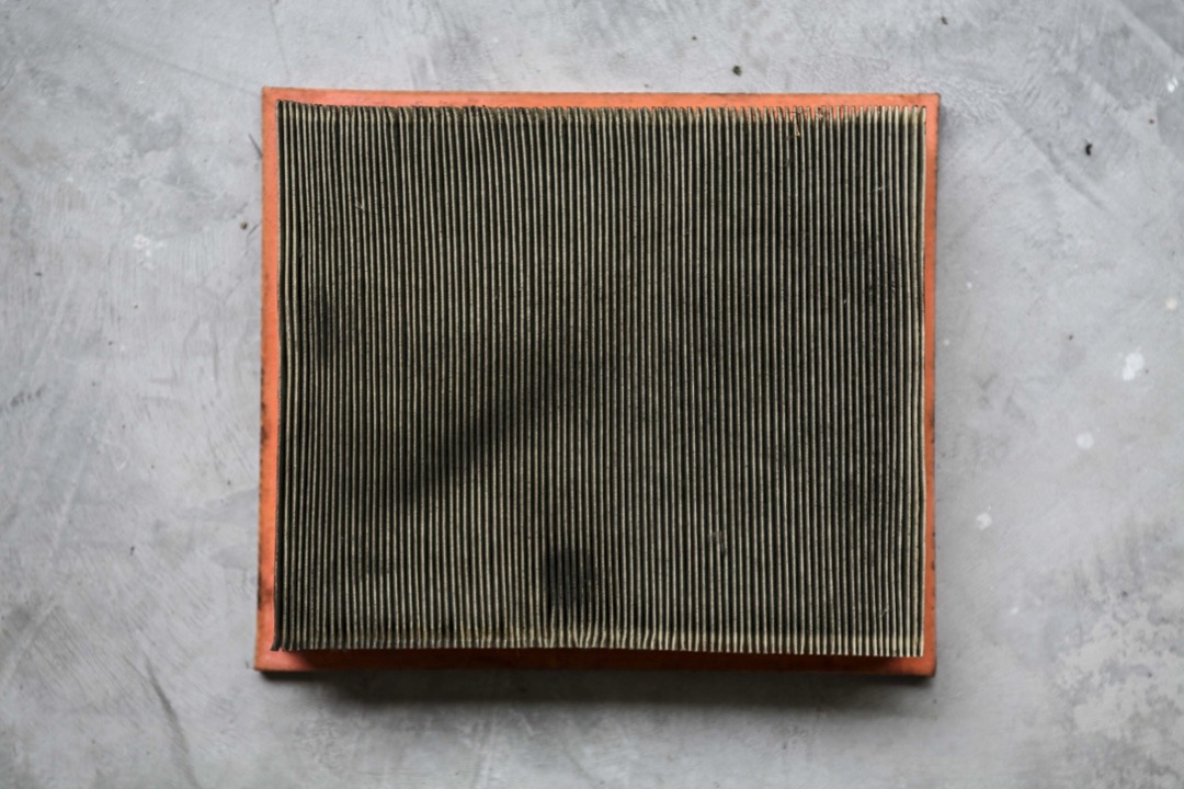 A used rectangular panel engine air filter with visible dirt loading across the pleats, removed from a car's airbox