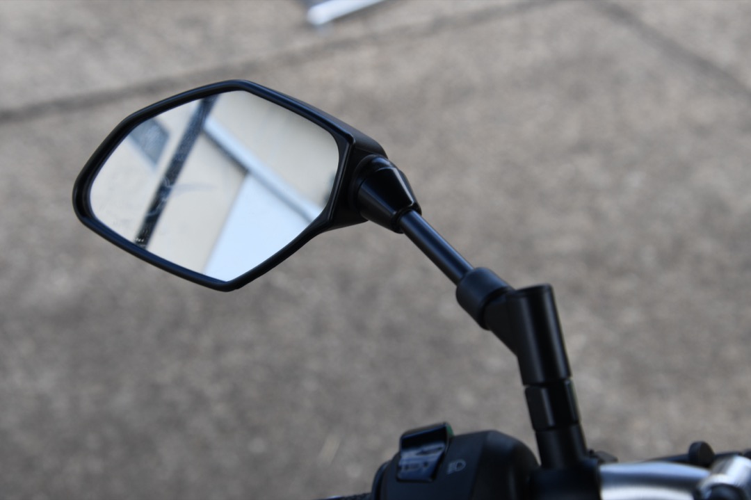 Close-up of a motorcycle left side mirror mounted on the handlebar stalk