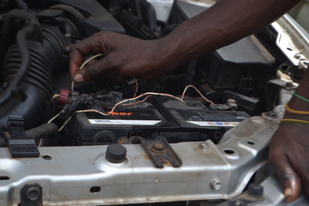 Mechanic in a spring service bay inspecting the undercarriage of a car with a flashlight, checking for salt corrosion on brake lines and frame seams after winter