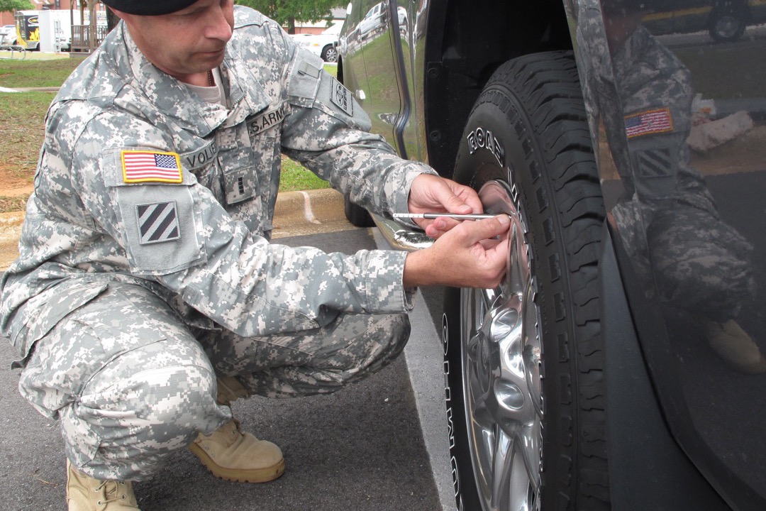 Close-up of a person checking tire pressure on a car wheel with a tire pressure gauge at the valve stem