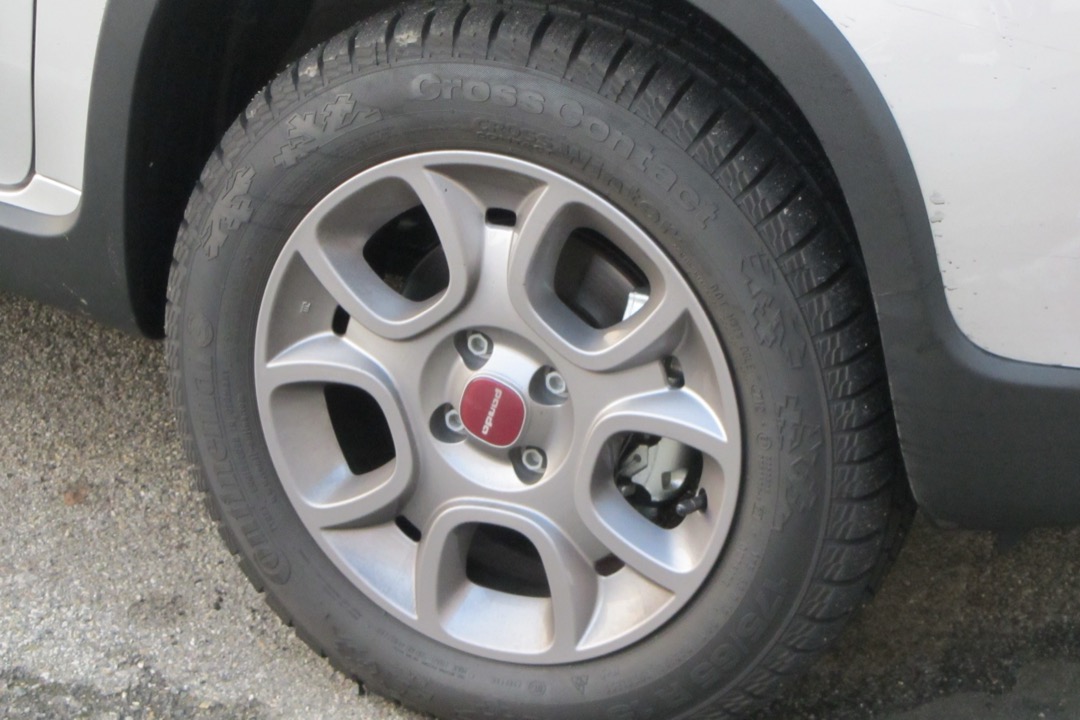 Winter tire with directional snow tread mounted on an alloy wheel of a compact car, showing the sidewall markings that identify a cold-weather tire